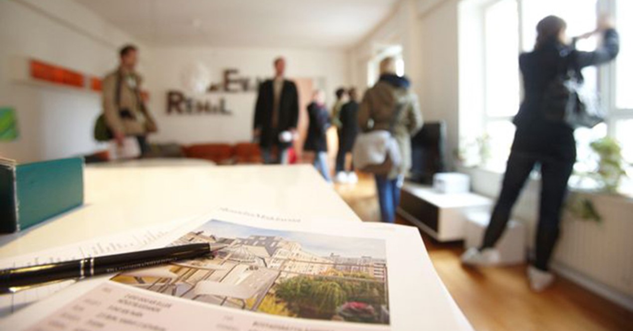 Nærbilde av en boligannonse i forgrunnen med flere personer på visning i bakgrunnen