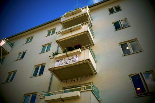 Bilde av bygård med et banner hengende fra balkongen, det det står "Reduser husleia" 