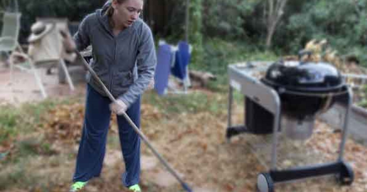 Person som raker i en hage fylt av løv.